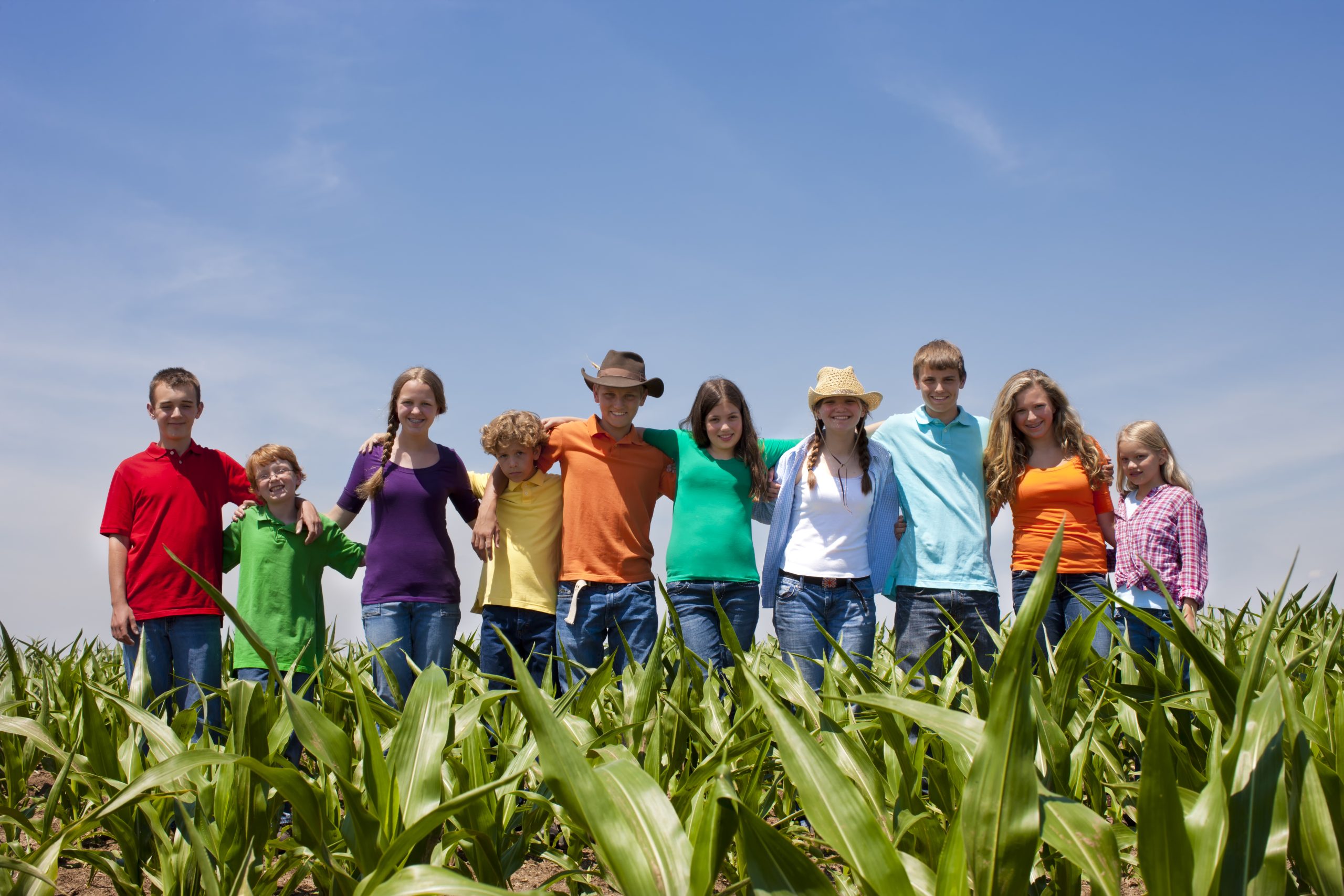 A team of hardworking children and teens stand proudly in a cornfield on an American farm.
